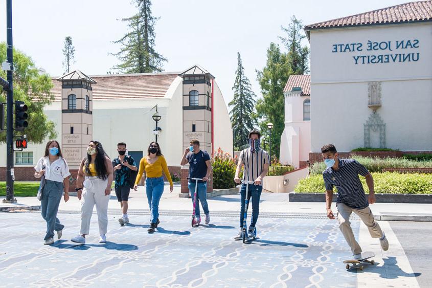 Students crossing the street and 一个 skateboarding with masks on.