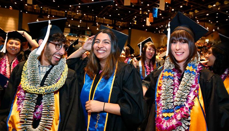 Three graduating students pose in their regalia under the glittering lights of the arena.