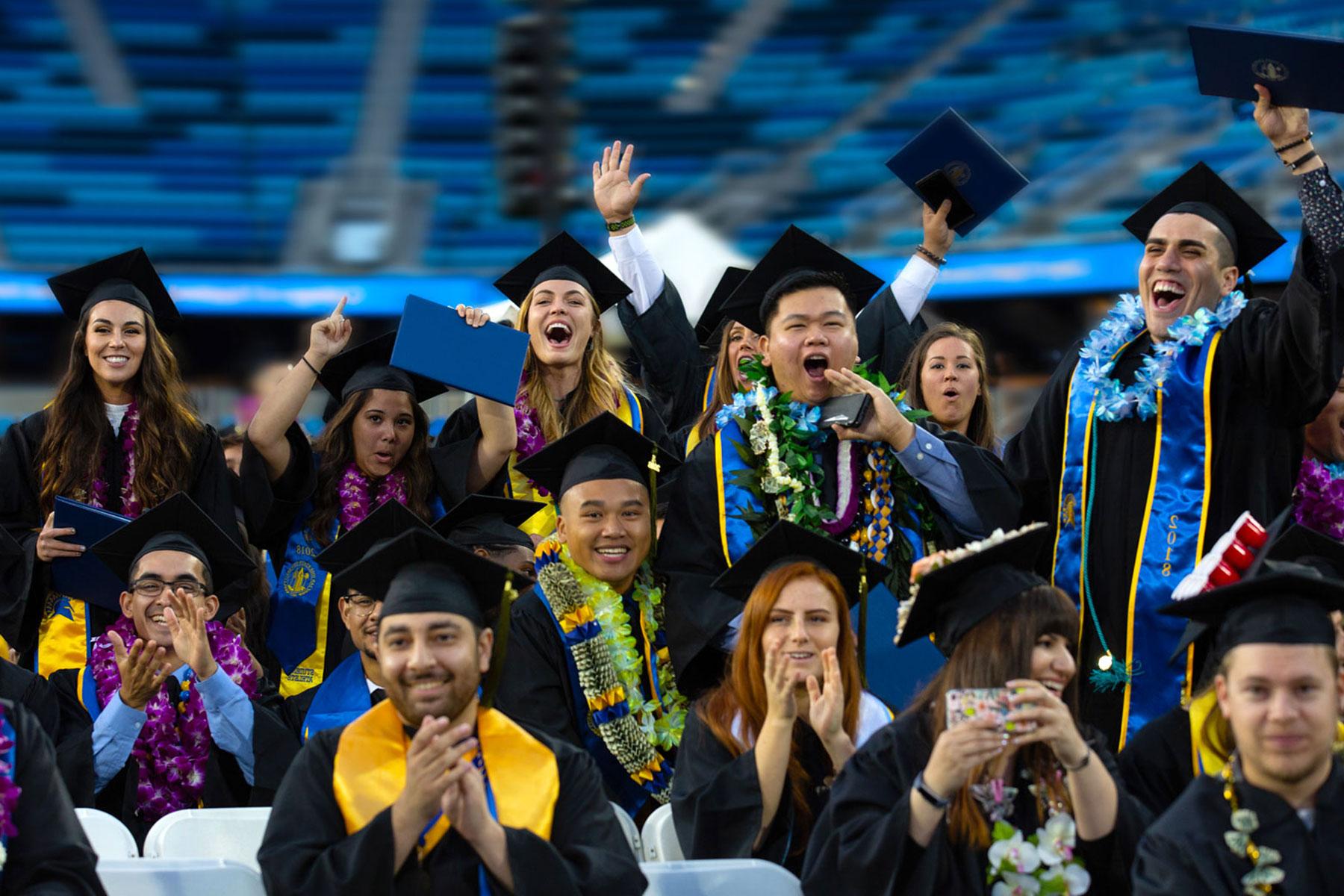 Graduates cheering in their caps and gowns.