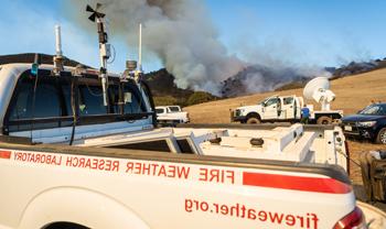 truck from the wildfire center sits in open field with wildfire in the distance.  measuring equipment is all around