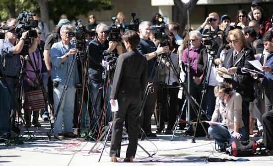 person speaks in front of tons of media people with cameras