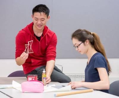 学生们一起工作.  One sits at table, 一个 sits on table.  they work with wood pieces and glue.